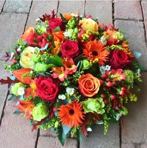Autumnal funeral posy in oranges and rusts, seasonal flowers set in floral foam for a graveside tribute