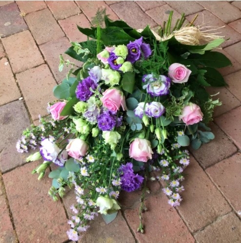 Hand tied funeral sheaf of seasonal flowers in soft colours, finished with ribbon