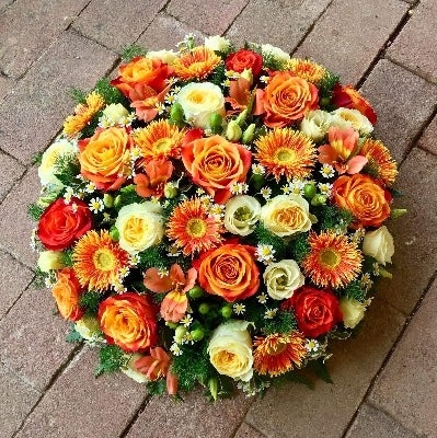 Posy pad of orange and lemon coloured seasonal flowers set in floral foam