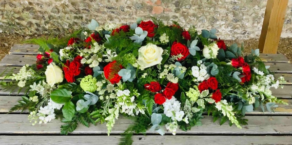 Red and white casket spray of roses and seasonal flowers arranged along the casket top