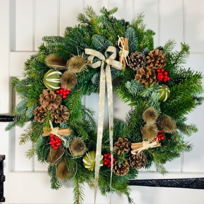 Opulent Christmas wreath of mixed evergreen foliage dressed with red berries, cones and gold accents, made at a Weyhill wreath workshop