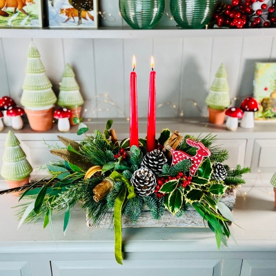 Christmas table centrepiece with red candles, pine cones, holly and berries on a festive dressed table