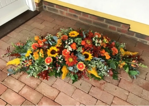Autumnal casket spray in oranges and russets arranged along the casket top