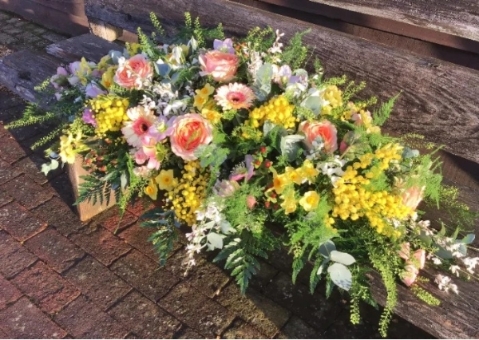 Apricot and yellow casket spray with roses and seasonal blooms, arranged for a funeral service