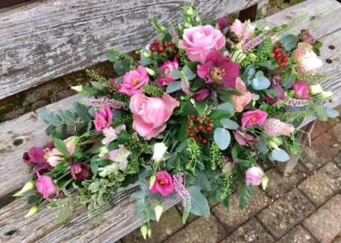 Pink and cranberry casket spray of roses and seasonal flowers with soft foliage