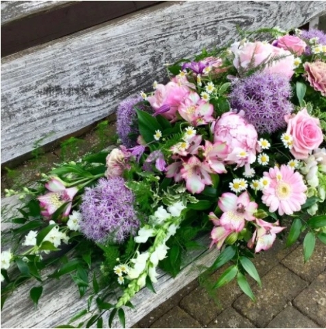 Pink and lilac casket spray of roses, lisianthus and seasonal flowers for a funeral service