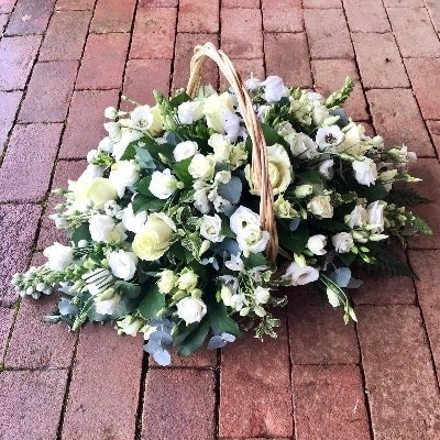 Funeral basket of mixed fresh flowers in soft colours, arranged in floral foam for the service