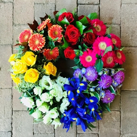 Rainbow funeral wreath with bands of red, orange, yellow, green, blue and purple flowers